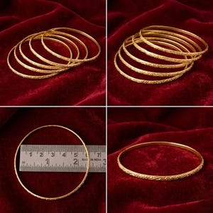 May include: Several gold-coloured bangles with textured patterns are presented on a red velvet backdrop. The image includes stacks of bangles and individual pieces, with a ruler showing the size. The bangles feature an intricate design.