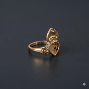 Puede incluir: Un anillo dorado con un relicario en forma de corazón que se abre. El anillo presenta una banda y un compartimento en forma de corazón que se abre para revelar un interior hueco. El relicario está articulado y tiene un diseño detallado. El anillo está sobre un fondo oscuro.