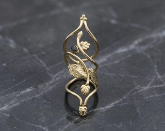 May include: A gold ring with an elaborate, swirling design. The ring has a black gemstone and leaf-like details. The ring's design is approximately 7.6 cm in height.
