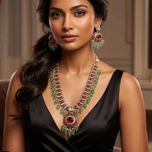 Peut inclure: Une femme porte un ensemble de collier et de boucles d'oreilles assortis. Les bijoux présentent des pierres précieuses rouges et vertes serties dans de l'or. Le collier a un grand pendentif avec une pierre rouge centrale. La femme porte une robe noire.