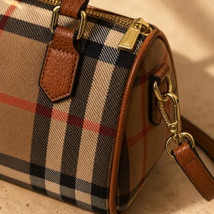 Puede incluir: Bolso de mano a cuadros marr&oacute;n y beige con detalles en cuero marr&oacute;n. El bolso presenta una cremallera y herrajes dorados, una correa para el hombro desmontable y un asa superior. El estampado a cuadros incluye rayas negras y rojas.