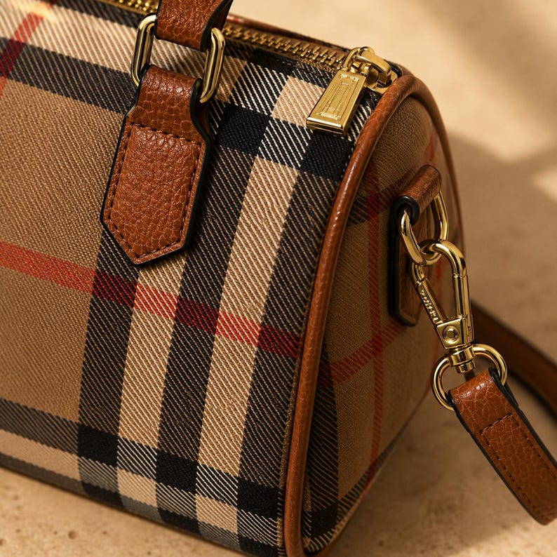 Puede incluir: Bolso de mano a cuadros marr&oacute;n y beige con detalles en cuero marr&oacute;n. El bolso presenta una cremallera y herrajes dorados, una correa para el hombro desmontable y un asa superior. El estampado a cuadros incluye rayas negras y rojas.