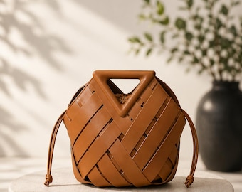 Bolsa tipo saco em couro vegano trançado marrom, com alça triangular, estilo boho.