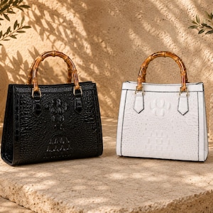 May include: Two structured handbags, one in black and one in white, both featuring a textured crocodile-embossed finish and a distinctive bamboo-style top handle. Each bag has a rectangular silhouette with gold-toned hardware attachments.