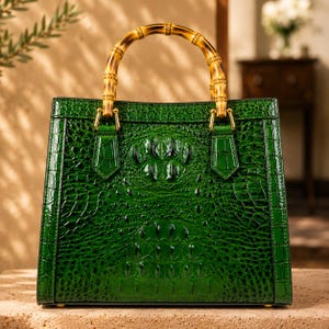 May include: A structured handbag in a deep emerald green color featuring a glossy, embossed crocodile skin texture. The bag is equipped with a curved, natural bamboo handle attached with gold-toned metal hardware, creating a distinct contrast.