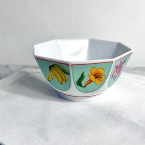 以下が含まれることがあります： 八角形の白いセラミックボウル。ボウルは、バナナ、黄色い花、紫の花のイラストが描かれたターコイズのボーダーが特徴です。縁は赤い線でトリミングされています。