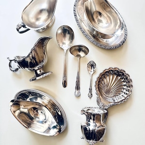 May include: An assortment of vintage silver serving pieces, including gravy boats, serving spoons, and decorative dishes. The pieces have a polished, reflective surface, showcasing intricate details and elegant designs. A collection of classic tableware.