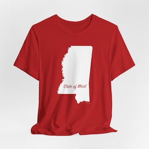 Puede incluir: Una camiseta roja con un contorno blanco del estado de Mississippi. El texto "State of Mind" está impreso en cursiva debajo del contorno del estado. La camiseta está hecha de un material suave.
