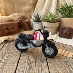 May include: A handmade crochet motorcycle in black, gray, red, and white. The amigurumi motorcycle has a detailed design, including wheels, handlebars, and a seat. A small tag reads "Handmade Motorcycle Amigurumi - Unique Gift -."