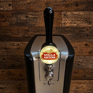 May include: A black and silver beer draft system with a Stella Artois logo on the tap handle. The system has a digital display and a drip tray. The text "Perfect Draft" is visible.