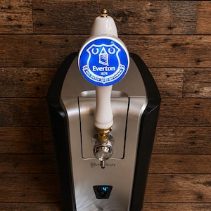 May include: A black and silver Perfect Draft beer dispenser with an Everton logo on the tap. The tap handle is white with gold accents. The dispenser has a digital temperature display and a drip tray.