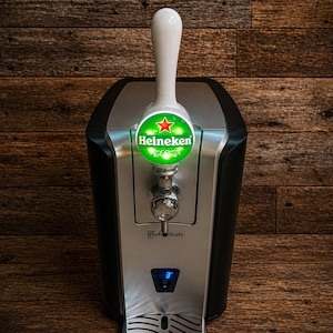 May include: A black and silver Perfect Draft beer dispenser with a white tap handle. The dispenser features a Heineken logo and a digital display. The background is a wooden surface.