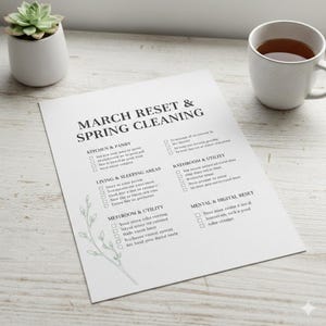May include: A printed checklist titled "MARCH RESET & SPRING CLEANING" with categories like Kitchen & Pantry, Living & Sleeping Areas, and Bathroom & Utility. A small succulent in a white pot and a mug of tea are also present.