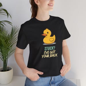 May include: Black t-shirt with a yellow cartoon duck and orange beak. The text "STUCK? I'VE GOT YOUR BACK" is below the duck. The shirt is made of a soft material.