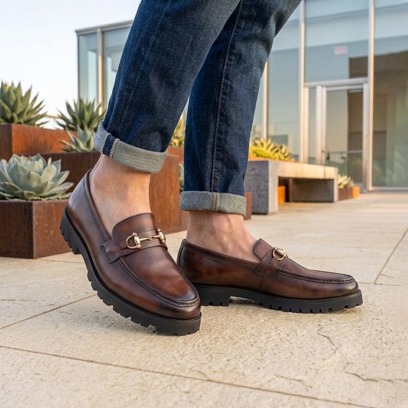 Mens brown full grain leather slip on loafer with black lug sole styled with cuffed jeans on a rooftop