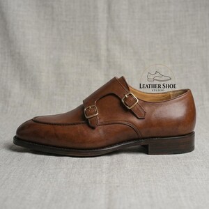 Mens cognac leather monk strap dress shoes with brass buckles close up
