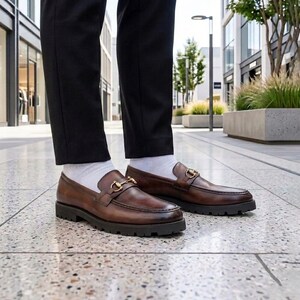 Product shot of dark brown men's leather horsebit loafers with thick rubber lug outsole on white background