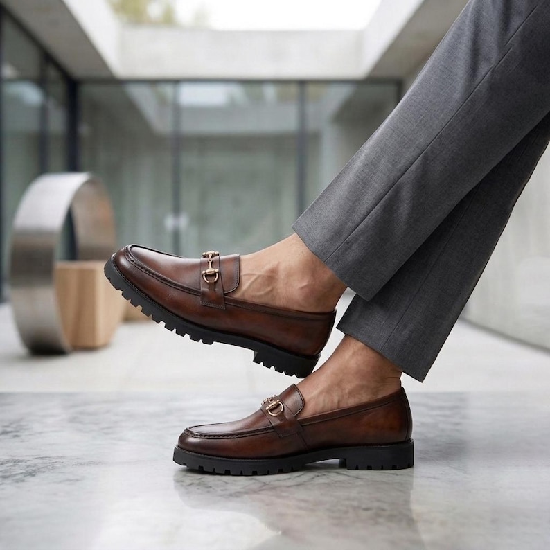 Brown patina leather men's loafer with gold horsebit worn with black dress trousers on a city plaza