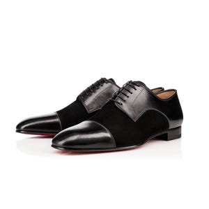 Può includere: Un paio di scarpe eleganti in pelle nera e camoscio con design a punta. Le scarpe hanno una chiusura con lacci e una suola rossa. Le scarpe sono esposte su sfondo bianco.