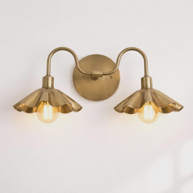 Elegant vintage brass double sconce brightens mirror areas beautifully

Scalloped metal shades create warm farmhouse ambience

Perfect vanity lighting for bathrooms hallways bedrooms

Stylish gold fixture supports glowing edison bulbs

Durable craftsmanship delivers timeless decorative interior accent