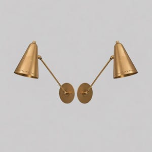 May include: A pair of matching wall-mounted lamps featuring conical brass shades with perforated detailing along the bottom edge. Each lamp has a slender adjustable arm extending from a circular brass wall plate, finished in a brushed metallic tone.