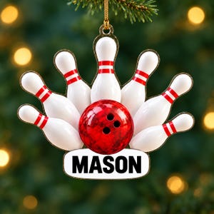May include: A hanging ornament featuring a red bowling ball centered in front of seven white bowling pins with red stripes. Below the bowling ball is a white rectangular plaque with the name MASON printed in bold black capital letters.