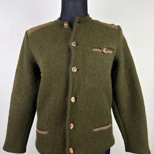 May include: Olive green wool jacket with a stand-up collar and wooden buttons. The jacket features brown suede shoulder patches and pocket trim. A classic, tailored garment.