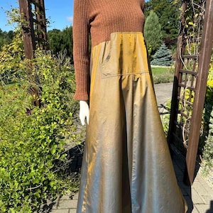 May include: A long dress featuring a brown ribbed knit long-sleeved bodice and a contrasting metallic gold and bronze iridescent skirt. The skirt includes a large front patch pocket and a full, flowing silhouette that reaches the floor.