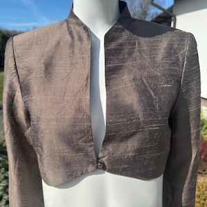 Puede incluir: Una taza de cerámica blanca con un asa negra y el texto "But First, Coffee" en negrita negra. La taza se encuentra sobre un fondo neutro, resaltando su diseño simple.