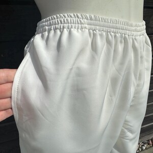Op de afbeelding: Close-up van een witte sportbroek met een elastische tailleband en zijzakken. De broek is gemaakt van een gladde, lichtgewicht stof. De broek wordt getoond op een mannequin.