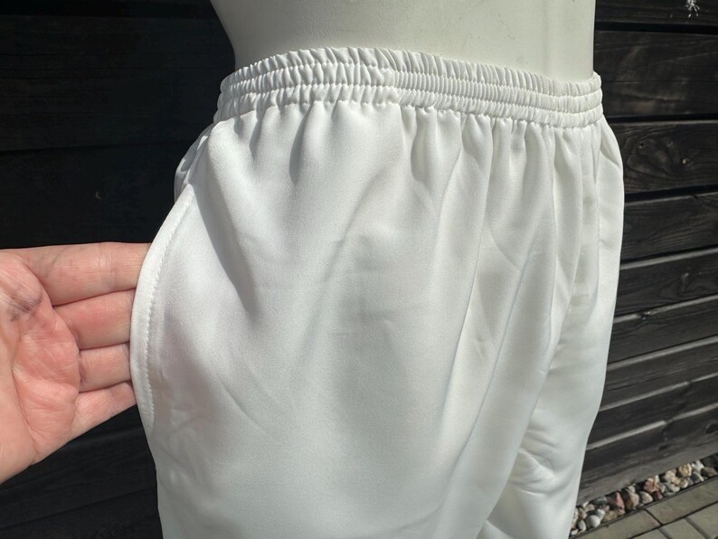 Op de afbeelding: Close-up van een witte sportbroek met een elastische tailleband en zijzakken. De broek is gemaakt van een gladde, lichtgewicht stof. De broek wordt getoond op een mannequin.