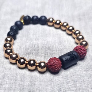 Peut inclure: Un bracelet de perles composé de perles de lave noire, de perles métalliques couleur or rose et de deux perles rouges sculptées. Une perle cylindrique noire avec un motif sculpté est également incluse.