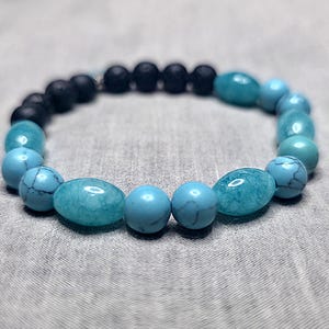 May include: A bracelet made of turquoise and black beads. The bracelet features a mix of round and oval turquoise beads, combined with smaller, round black beads. The beads are strung together, creating a fashionable accessory.