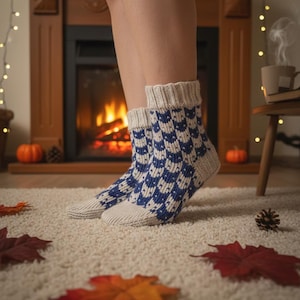 May include: Cozy, patterned socks in blue and white, with a geometric design. The socks are knit with a cream-colored toe and cuff. The socks are worn indoors near a fireplace, with fall decorations.