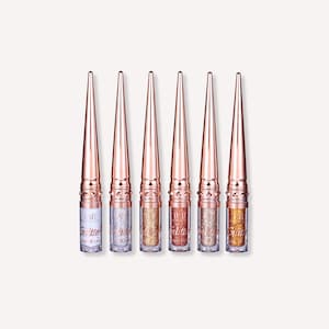 May include: Six glitter liquid eyeliners with rose gold caps and applicators. The bottles contain silver, gold, and bronze glitter. The text "Glitter Liquid Liner" is printed on the bottles.