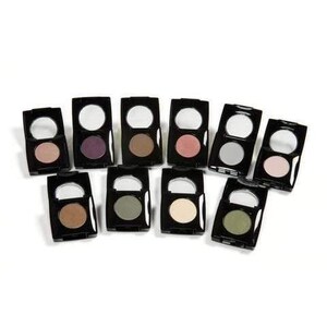 May include: An assortment of eyeshadow palettes in black compacts. Each palette contains a round mirror and a single eyeshadow in various colors, including pink, purple, brown, and green. The palettes are arranged on a white surface.