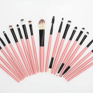 May include: A collection of makeup brushes arranged in a semi-circle. The brushes have pink handles and black bristles. The set includes various brush sizes and shapes for different makeup applications.
