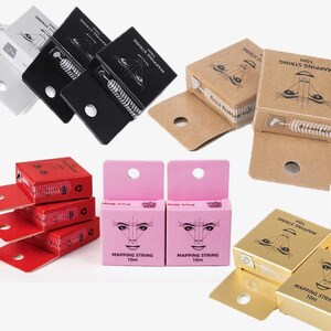May include: Assortment of mapping string boxes in various colors, including black, brown, red, pink, and gold. Each box features a diagram of a face and the text "MAPPING STRING 10m". The boxes are designed for professional use.