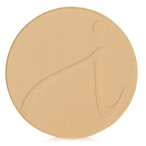 Könnte beinhalten: Ein runder, hellbeige Make-up-Kompaktpuder mit strukturierter Oberfläche. Der Kompaktpuder hat ein stilisiertes "i"-Design. Das Erscheinungsbild ist sauber und schlicht, was auf den Fokus auf das Produkt selbst hindeutet.