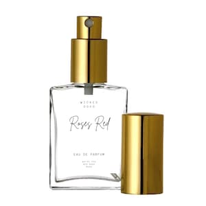 May include: A clear glass perfume bottle with a gold-colored cap and sprayer. The bottle has the words "WICKED GOOD" and "Roses Red" printed on it. The fragrance is described as "EAU DE PARFUM" with notes of white tea, red rose, and musk.
