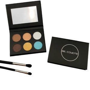 May include: A black eyeshadow palette with six shades of eyeshadow in brown, beige, white, yellow, and blue. The palette has a mirror and is open, next to a closed black case with the text "BE. COYOTE". Two black makeup brushes are also present.