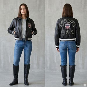 Puede incluir: Chaqueta de cuero negra con ribetes a rayas blancas y negras, con un parche en el pecho y el texto "AVIREX USA" en la espalda. La chaqueta se combina con vaqueros azules y botas altas negras.