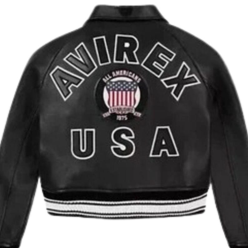 Puede incluir: Chaqueta de cuero negra con letras blancas que dicen "AVIREX" y "USA". La chaqueta presenta un parche con la bandera estadounidense y las palabras "ALL AMERICANS" y "1975". La chaqueta tiene un dobladillo a rayas blancas y negras.