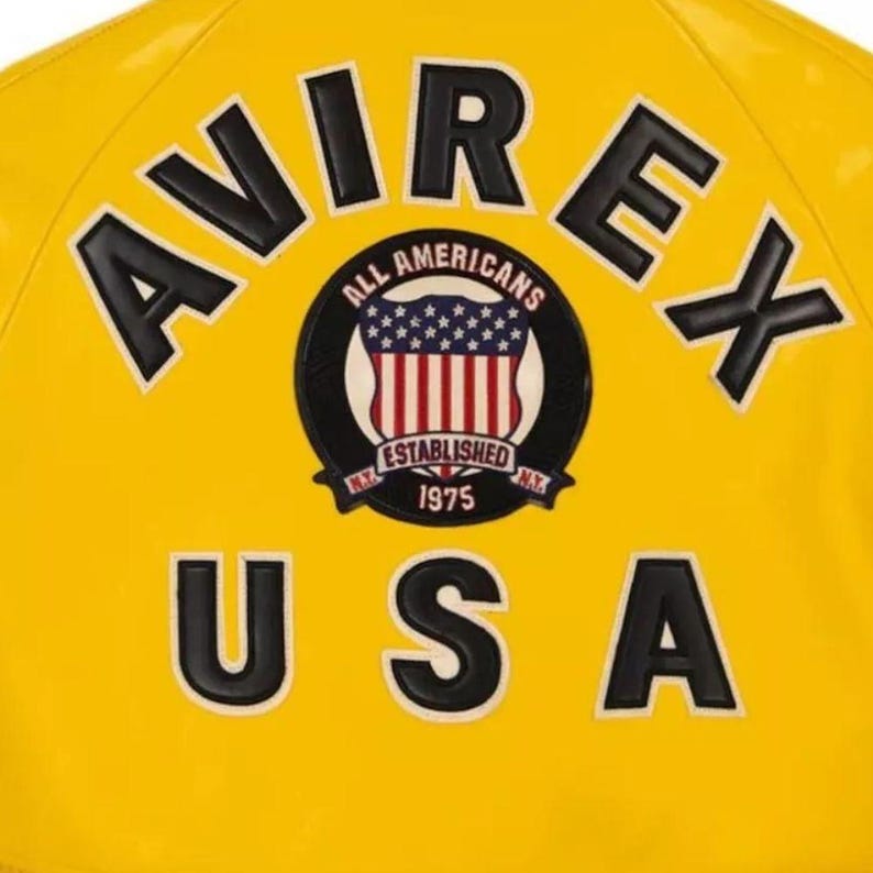 May include: A yellow jacket with black and white lettering and patches. The jacket displays the text "AVIREX" and "USA". A circular patch shows "ALL AMERICANS" and "ESTABLISHED 1975" with a US flag design.