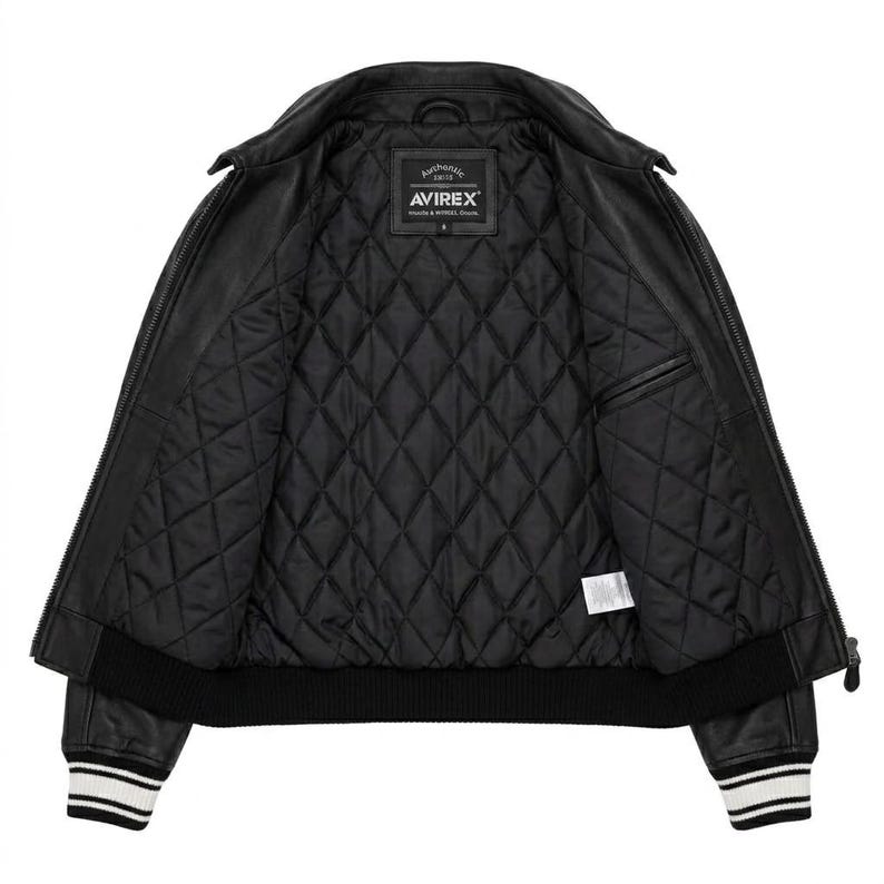 Puede incluir: Chaqueta de cuero negra con interior acolchado. La chaqueta presenta un cuello cl&aacute;sico, cierre de cremallera y pu&ntilde;os acanalados con rayas blancas. El forro interior es negro y acolchado con rombos. La etiqueta de la marca "AVIREX" es visible.