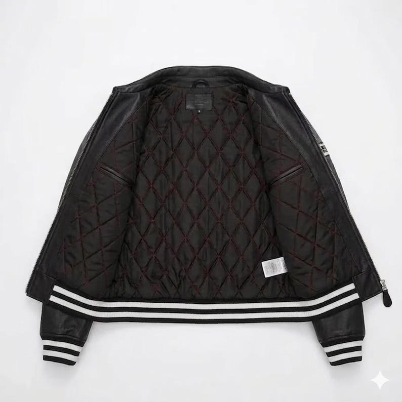 May include: Black leather jacket with a quilted, burgundy-lined interior. The jacket features a zipper closure, two front pockets, and white stripes on the cuffs and hem. A classic outerwear piece.