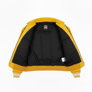 May include: Open yellow bomber jacket with a black interior. The jacket has a ribbed collar, cuffs, and hem with white stripes. The jacket has a zipper closure and a small logo patch on the inside.