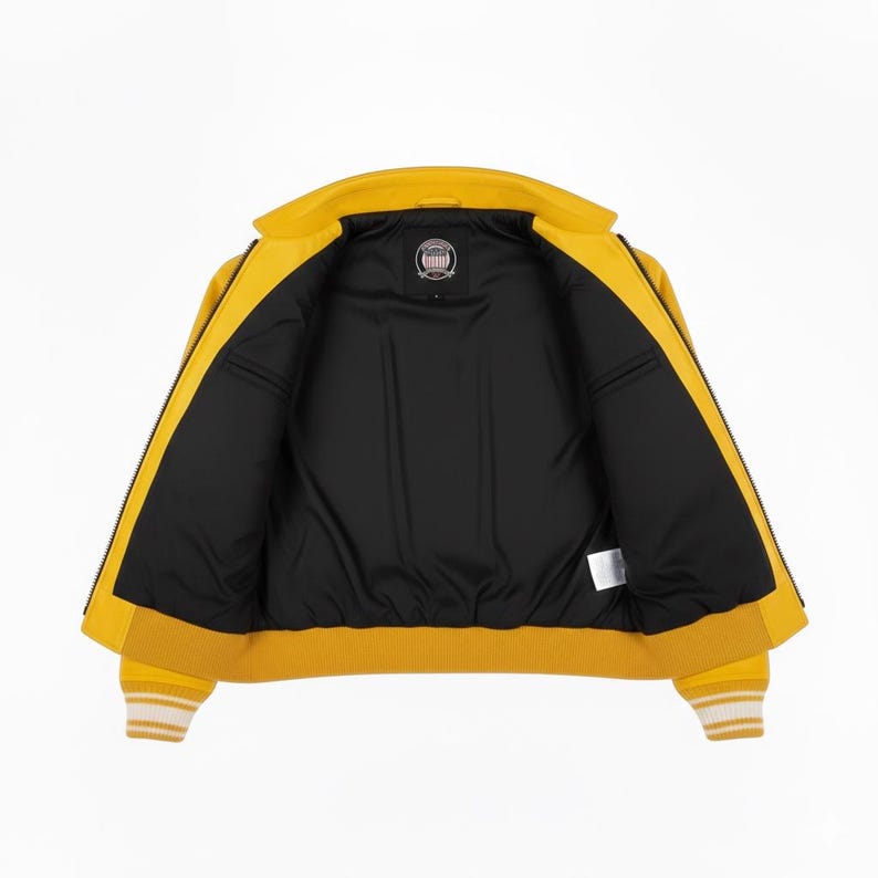 May include: Open yellow bomber jacket with a black interior. The jacket has a ribbed collar, cuffs, and hem with white stripes. The jacket has a zipper closure and a small logo patch on the inside.