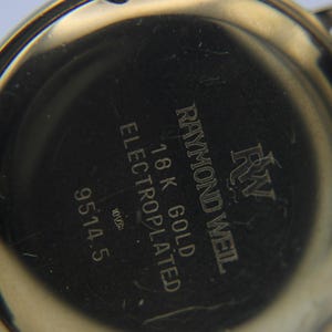 Close-up of the watch's gold case back, showing engravings for 'Raymond Weil', '18K GOLD ELECTROPLATED', and '9514.5'.