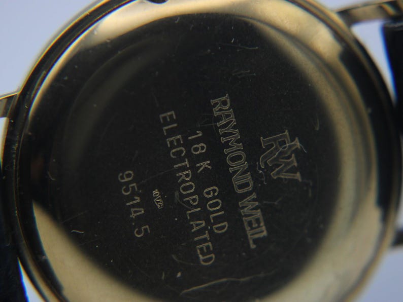 Close-up of the watch's gold case back, showing engravings for 'Raymond Weil', '18K GOLD ELECTROPLATED', and '9514.5'.